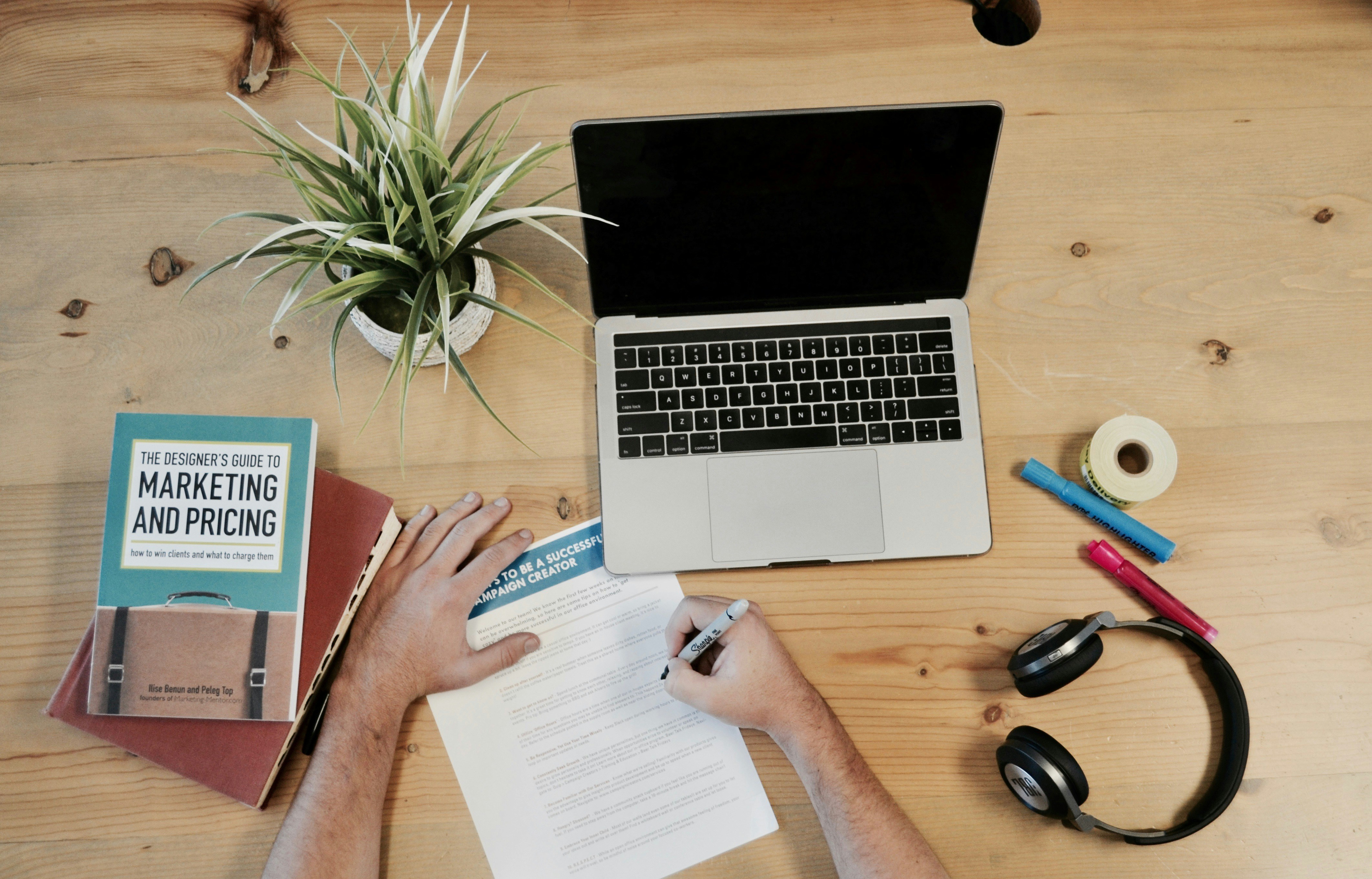 a hand writing on a piece of paper and a laptop on a table